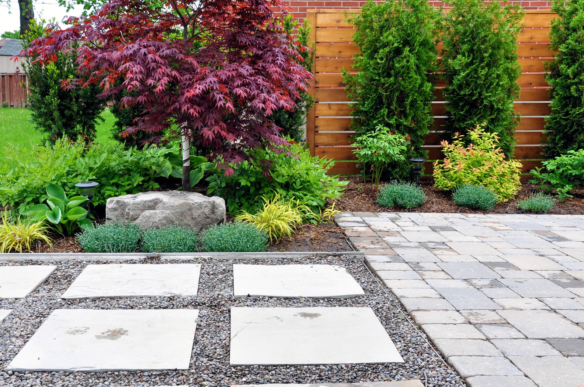 Hardscape details of a tumbled paver patio, flagstone stepping stones and horizontal cedar fence in a modern Japanese garden.